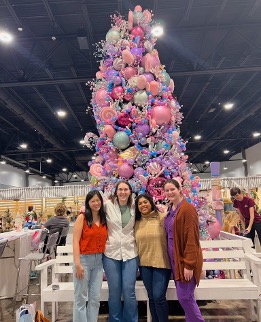 four residents standing in front of a large, pastel-themes Christmas tree at Mistletoe Marketplace